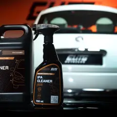 Dwa opakowania IPA CLEANER, alkohol izopropylowy do detailingu auta, stoją obok białego samochodu.