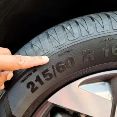 Palec wskazuje na oznaczenie opon 215/60 R16. Informacja ta jest kluczowa przy zakupie nowych opon.