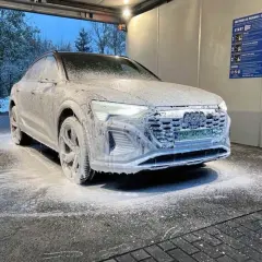 Audi pokryte pianą na myjni bezdotykowej zimą. Śnieg na drzewach w tle.