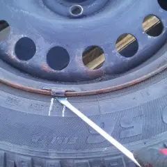 Rękawica w czerwonej rękawicy usuwa rdzę z felgi stalowej za pomocą narzędzia. To pierwszy krok, jak wyczyścić felgi stalowe z rdzy.