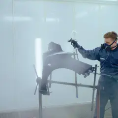 Lakierowanie akrylem krok po kroku: pracownik w masce i kombinezonie maluje element karoserii w kabinie lakierniczej.