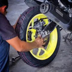 Mechanik pracuje nad wymianą opon motocyklowych, skupiając się na tylnym kole z żółtą felgą.