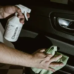 Ręce czyszczą wnętrze samochodu preparatem APC2. W tle widać klamkę i panel drzwi.