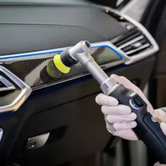 Ręce w rękawiczkach wykonują polerowanie plastiku w samochodzie za pomocą polerki.