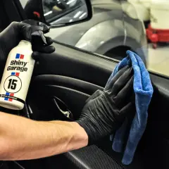 Ręce w czarnych rękawiczkach używają preparatu Shiny Garage Apple Dressing i niebieskiej mikrofibry, by dowiedzieć się, czym wyczyścić plastiki w samochodzie.