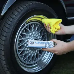 Ręce polerują felgi pastą K2 Aluchrom. Żółta ściereczka i opakowanie produktu podkreślają blask odnawianych felg.