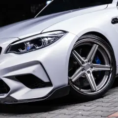 Białe auto z błyszczącymi, wieloramiennymi felgami i niebieskimi zaciskami hamulcowymi.