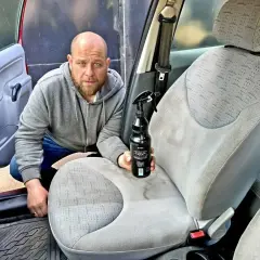 Mężczyzna z butelką środka czyszczącego pokazuje, czym wyczyścić samochód w środku domowe sposoby.