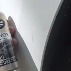 Butelka K2 VENOX do usuwania rys z lakieru obok widocznych zarysowań na białym samochodzie.