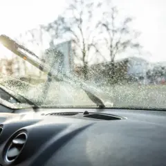 Widok z wnętrza samochodu na zaparowaną szybę i pracujące wycieraczki. Dowiedz się, jak myć szyby w samochodzie od wewnątrz, by zapewnić sobie dobrą widoczność.