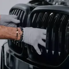 Ręce w rękawiczkach montują czarny grill w samochodzie.