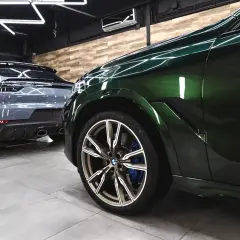 Błyszczące, zielone BMW i szary Porsche w profesjonalnym studiu auto detailing.