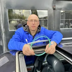 Mechanik z Audi A6 C6 pokazuje, jak udrożnić odpływ wody z podszybia. Używa do tego zielonego wężyka i szczoteczki.