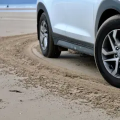 Białe auto na plaży, z widocznymi srebrnymi felgami. Zastanawiasz się, jaki kolor felg do białego auta będzie najlepszy? Te wyglądają świetnie!