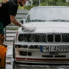 Mężczyzna myje białe BMW, stosując prewash. To pierwszy etap dokładnego czyszczenia auta, usuwający luźne zabrudzenia.