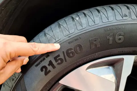 Palec wskazuje na oznaczenie opon 215/60 R16. Informacja ta jest kluczowa przy zakupie nowych opon.