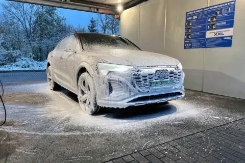 Audi pokryte pianą na myjni bezdotykowej zimą. Śnieg na drzewach w tle.