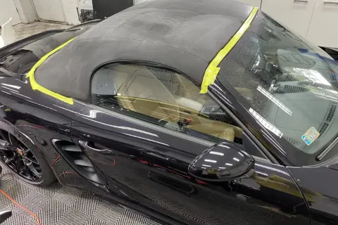 Czarny materiał na dach cabrio, zabezpieczony żółtą taśmą, gotowy do renowacji.