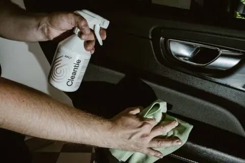 Ręce czyszczą wnętrze samochodu preparatem APC2. W tle widać klamkę i panel drzwi.
