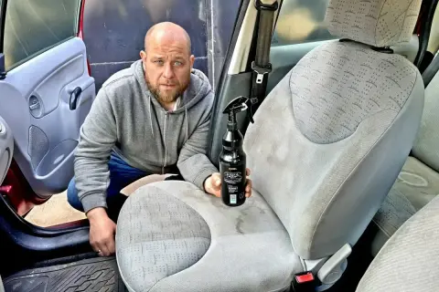 Mężczyzna z butelką środka czyszczącego pokazuje, czym wyczyścić samochód w środku domowe sposoby.