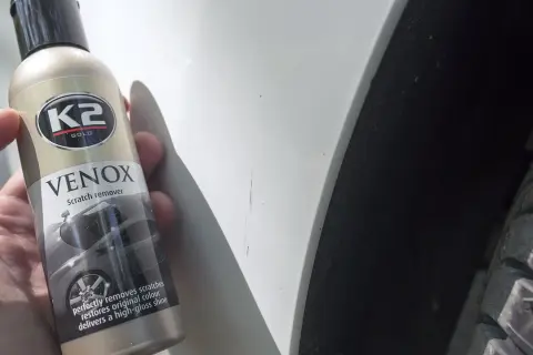 Butelka K2 VENOX do usuwania rys z lakieru obok widocznych zarysowań na białym samochodzie.
