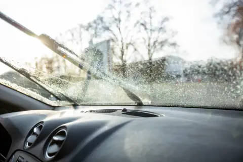 Widok z wnętrza samochodu na zaparowaną szybę i pracujące wycieraczki. Dowiedz się, jak myć szyby w samochodzie od wewnątrz, by zapewnić sobie dobrą widoczność.