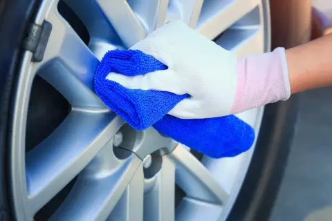 Ręka w białej rękawiczce czyści srebrną felgę niebieską ściereczką. Może to być część procesu czyszczenia felg WD40.