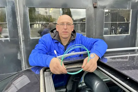 Mechanik z Audi A6 C6 pokazuje, jak udrożnić odpływ wody z podszybia. Używa do tego zielonego wężyka i szczoteczki.