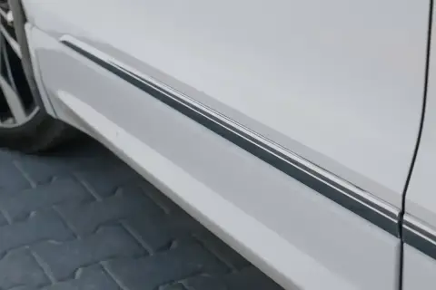 Usuwanie rys z chromu na listwie progowej białego samochodu.