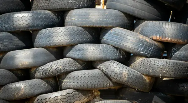 Stos starych opon, niektóre z widocznymi śladami zużycia i oznaczeniami, które mogą wskazywać na datę produkcji opony.