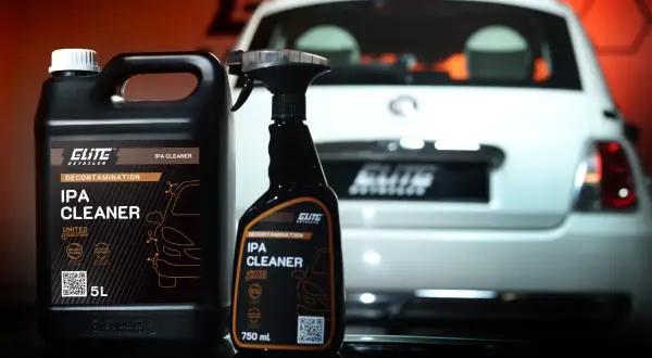 Dwa opakowania IPA CLEANER, alkohol izopropylowy do detailingu auta, stoją obok białego samochodu.