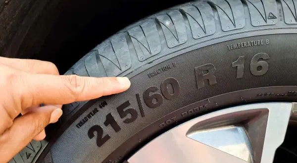 Palec wskazuje na oznaczenie opon 215/60 R16. Informacja ta jest kluczowa przy zakupie nowych opon.