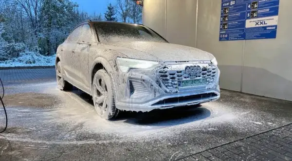 Audi pokryte pianą na myjni bezdotykowej zimą. Śnieg na drzewach w tle.