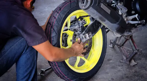 Mechanik pracuje nad wymianą opon motocyklowych, skupiając się na tylnym kole z żółtą felgą.