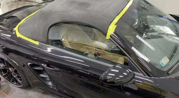 Czarny materiał na dach cabrio, zabezpieczony żółtą taśmą, gotowy do renowacji.