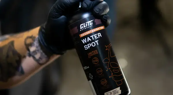 Ręka w czarnej rękawiczce trzyma butelkę preparatu "Water Spot" do usuwania water spotów na lakierze.
