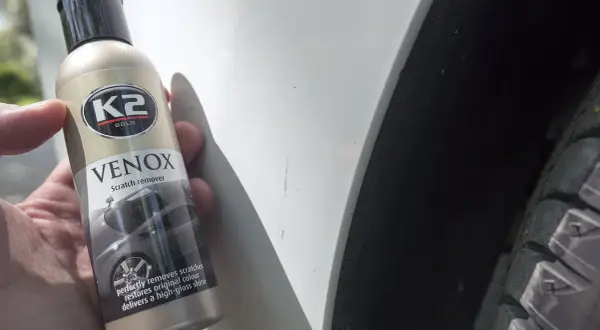 Butelka K2 VENOX do usuwania rys z lakieru obok widocznych zarysowań na białym samochodzie.