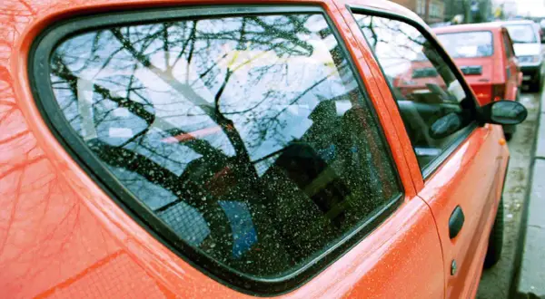 Widok na pomarańczowy samochód z widocznymi śladami żywicy na szybie. Zastanawiasz się, czym zmyć żywicę z szyby?