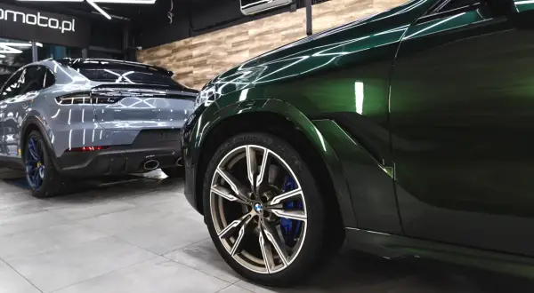 Błyszczące, zielone BMW i szary Porsche w profesjonalnym studiu auto detailing.
