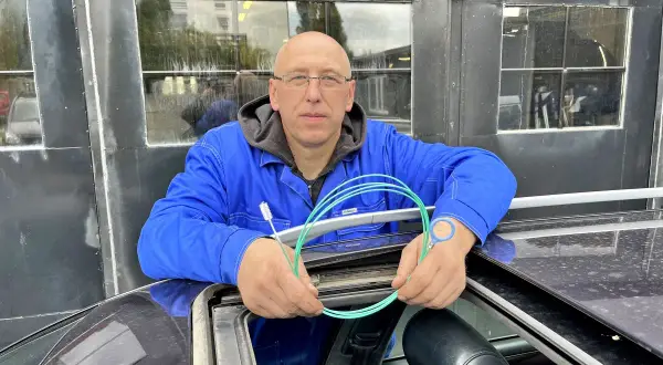 Mechanik z Audi A6 C6 pokazuje, jak udrożnić odpływ wody z podszybia. Używa do tego zielonego wężyka i szczoteczki.