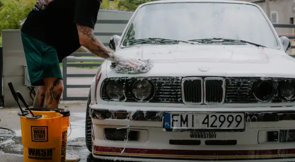Mężczyzna myje białe BMW, stosując prewash. To pierwszy etap dokładnego czyszczenia auta, usuwający luźne zabrudzenia.