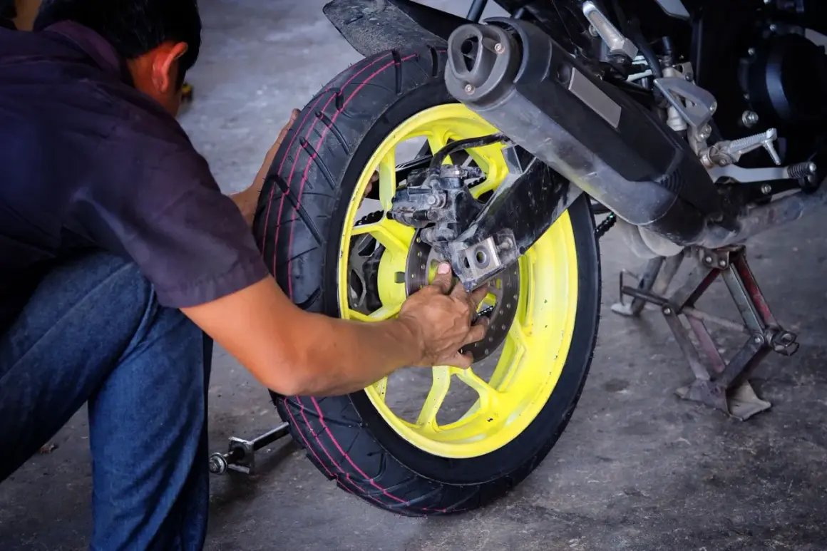 Mechanik pracuje nad wymianą opon motocyklowych, skupiając się na tylnym kole z żółtą felgą.