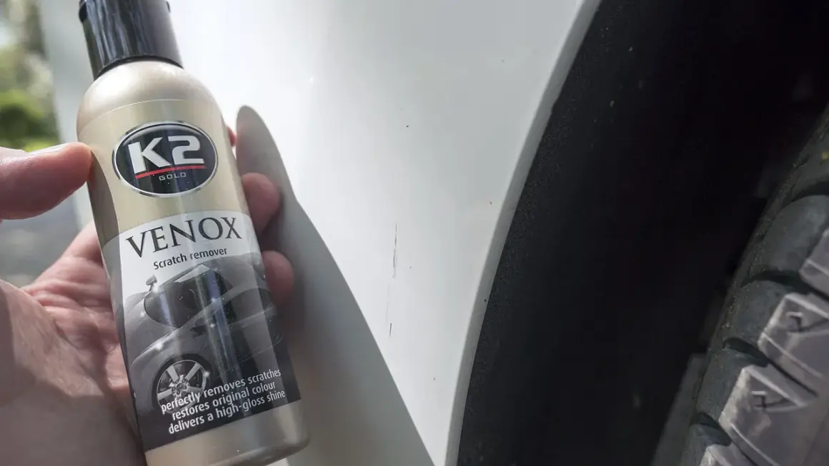 Butelka K2 VENOX do usuwania rys z lakieru obok widocznych zarysowań na białym samochodzie.