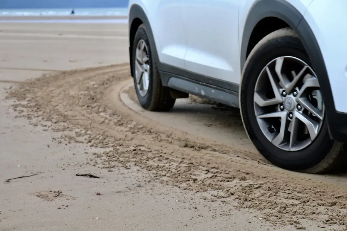 Białe auto na plaży, z widocznymi srebrnymi felgami. Zastanawiasz się, jaki kolor felg do białego auta będzie najlepszy? Te wyglądają świetnie!