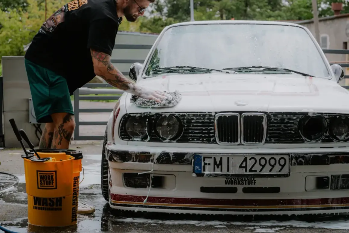 Mężczyzna myje białe BMW, stosując prewash. To pierwszy etap dokładnego czyszczenia auta, usuwający luźne zabrudzenia.