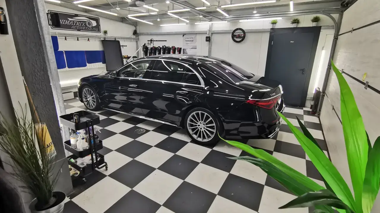 Profesjonalne wyposażenie studia detailingowego: czarny Mercedes S500 lśni na szachownicowej posadzce, otoczony narzędziami i kosmetykami.