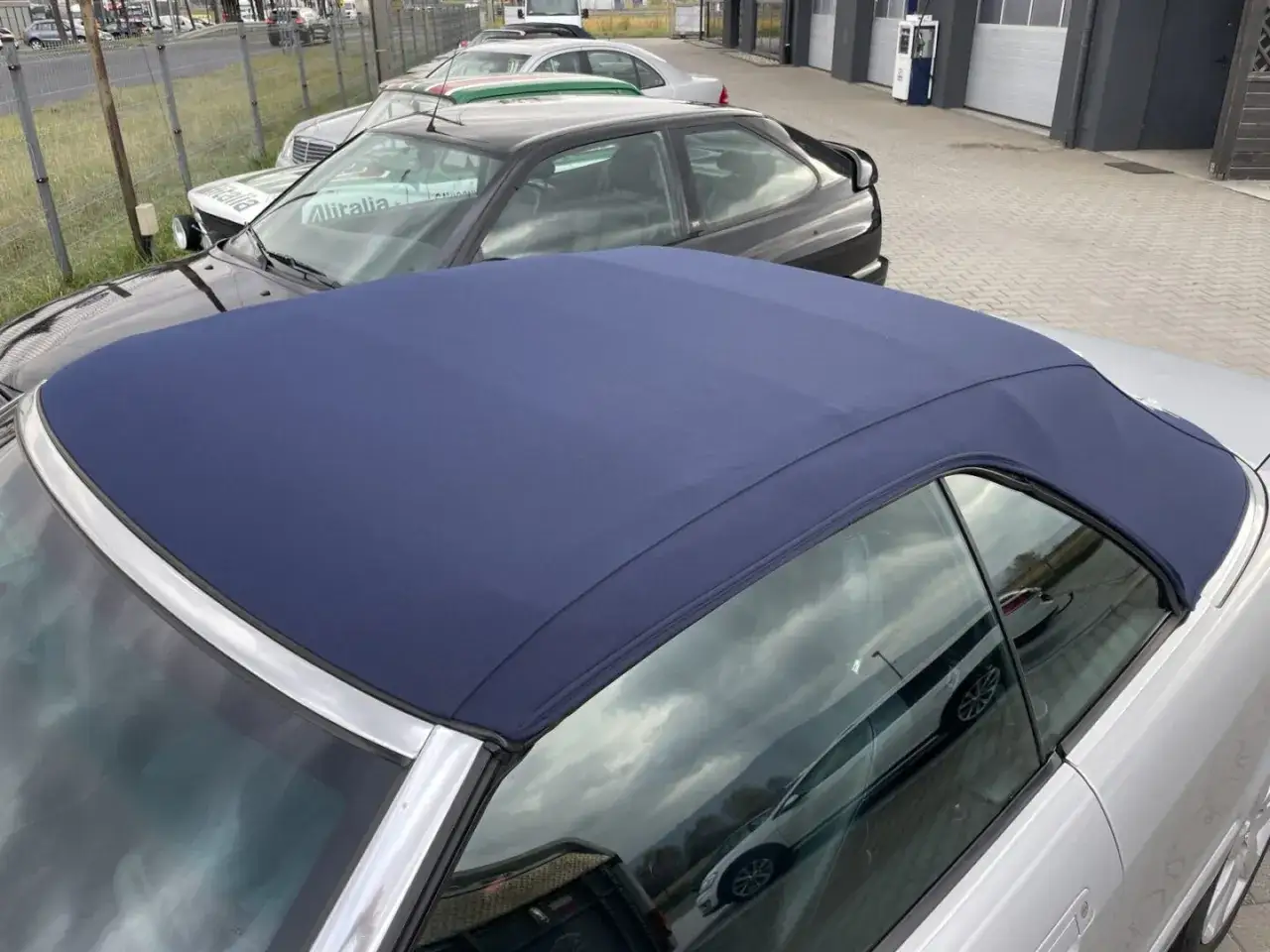 Granatowy dach cabrio na srebrnym samochodzie, w tle inne auta i budynki.