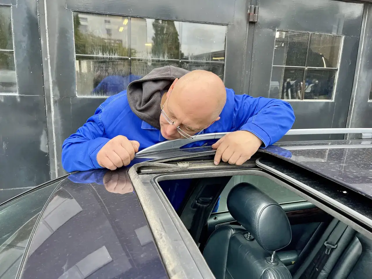 Mężczyzna w niebieskim kombinezonie sprawdza uszczelkę szyberdachu, szukając sposobu, jak udrożnić odpływ.