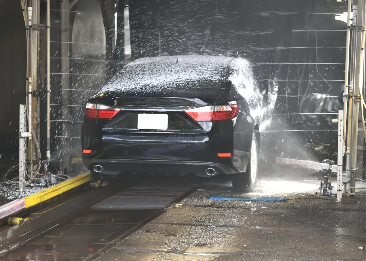 Czarny samochód w myjni automatycznej, gdzie pre-wash oprysk pokrywa go pianą.