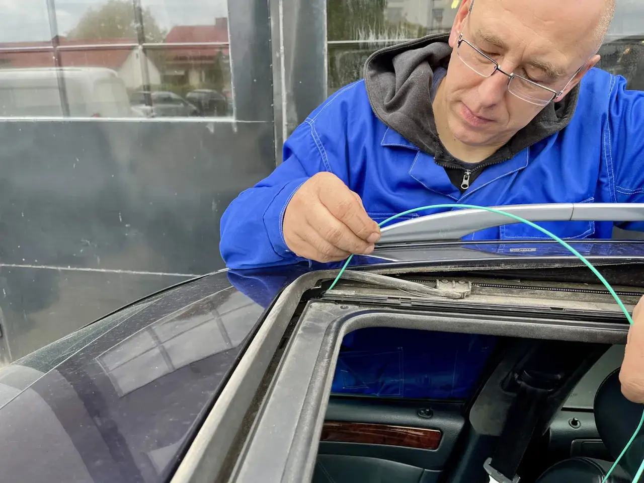 Mężczyzna w niebieskim kombinezonie udrażnia odpływ szyberdachu, używając zielonego przewodu.